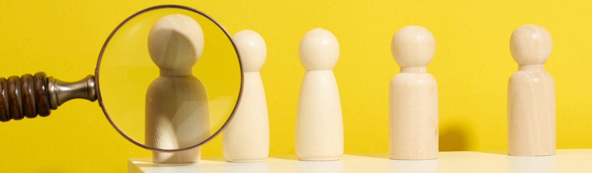 figurines of men on a white table and magnifying glass. Concept of searching for employees in the company, recruiting personnel, identifying talented and strong personaliti